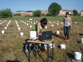 Dos colaboradoras del proyecto miden los recipientes con agua mediante un instrumento de precisión.